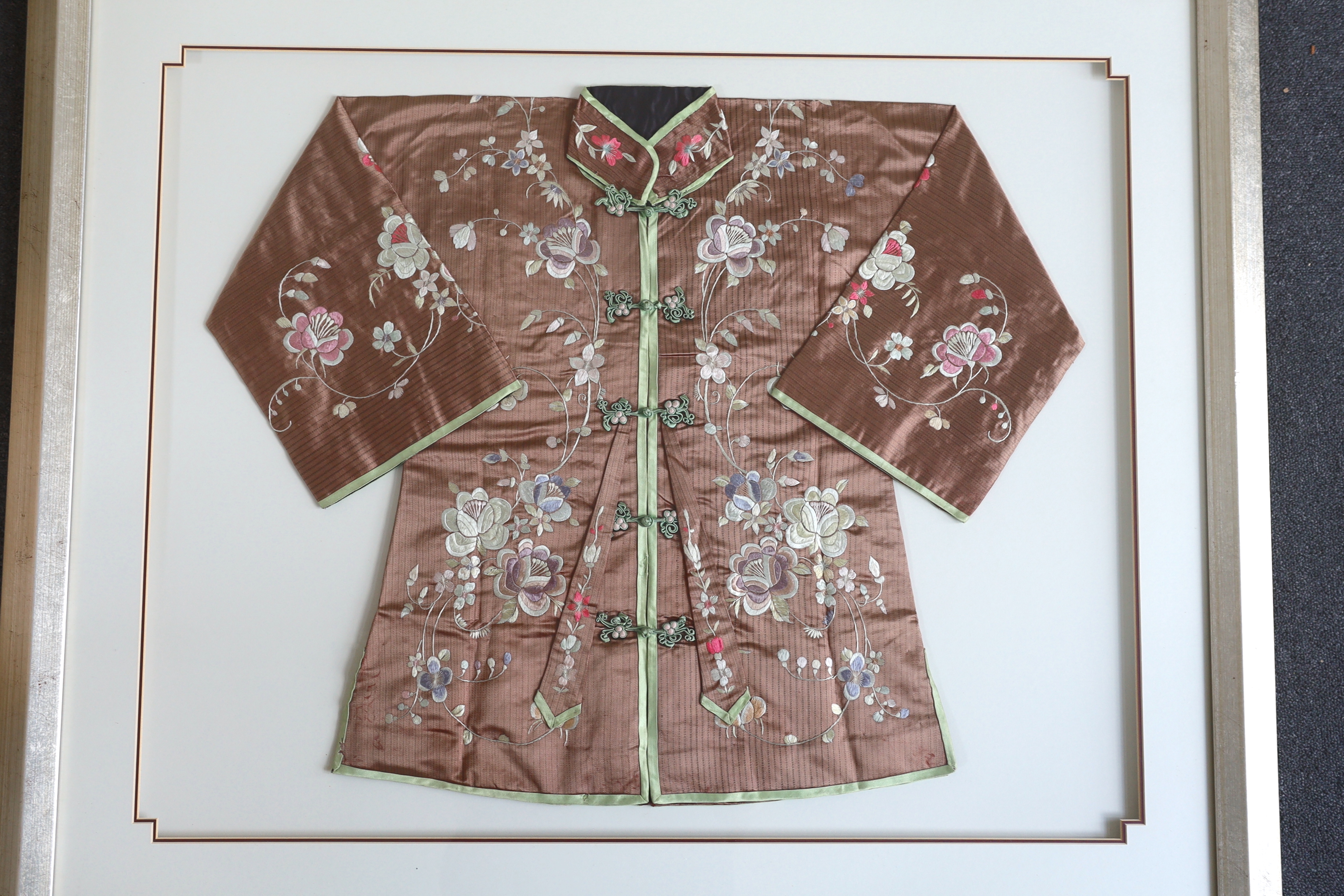 An early 20th century Chinese brown silk robe, with pastel multi-coloured all over embroidered flowers, framed and double mounted, measured as mounted: 75cm wide, 61cm high